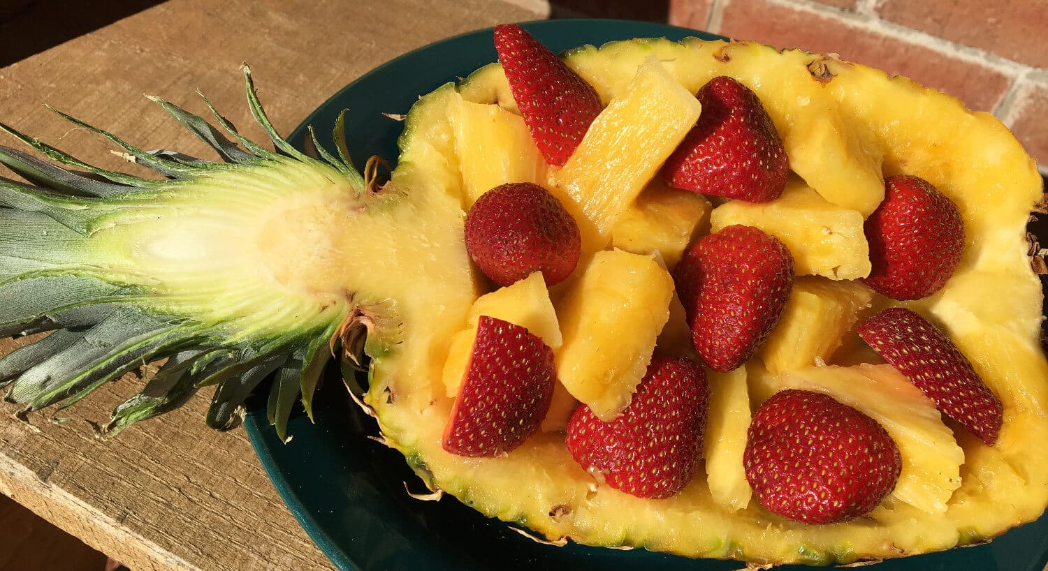 Half a pineapple filled with juicy yellow pineapple chunks and cut up red strawberries