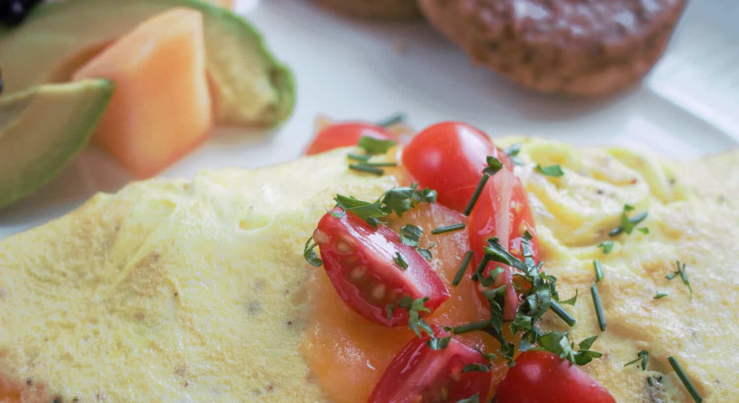 Omelet with tomatoes on top with fruit and sausage