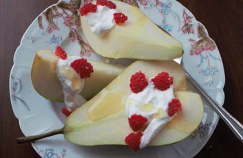 Cut pears with cream and raspberries on a china plate