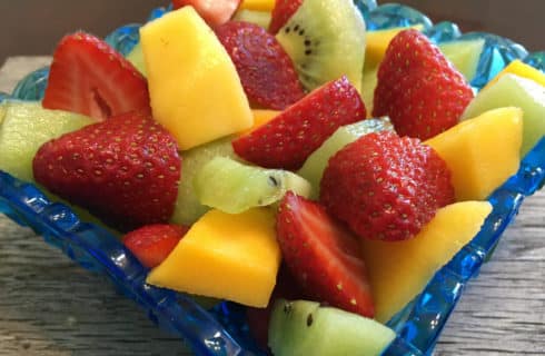Fresh cantaloupe and kiwi and strawberries in a blue glass bowl